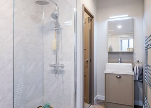 Ein modernes Badezimmer mit einer Duschkabine, einem Waschbecken mit Spiegel und einem Handtuchhalter.