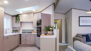 A modern kitchen with built-in appliances, a herringbone floor, and a small island with a plant. - Deluxe modern and contemporary luxury lodge perfect for a relaxing escape. (Workington)