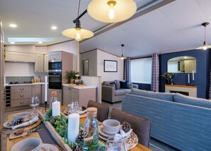 Eine moderne Küche mit integrierten Geräten, ein Essbereich mit Tisch für vier Personen und eine Wohnfläche mit Sofa und Kamin.
