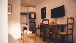 A compact kitchen with a dining area, a washing machine, and a flat-screen TV mounted on the wall.