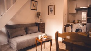 A cozy living room with a sofa, a small table with a bowl of fruit, and a staircase.