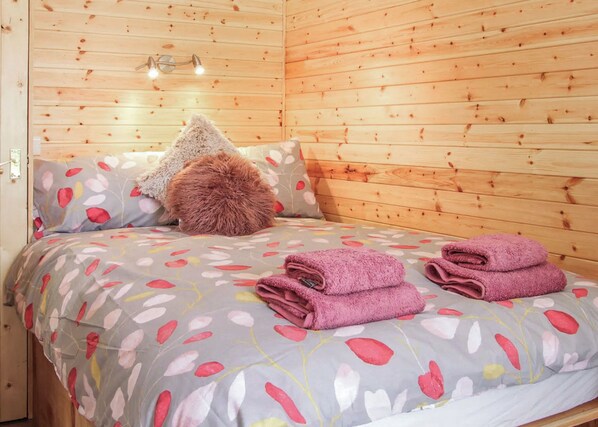 Una habitación de cabaña de madera con una cama, almohadas y una mesita de noche.