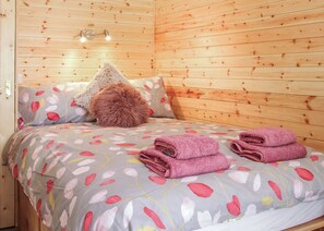 Una habitación de cabaña de madera con una cama, almohadas y una mesita de noche.