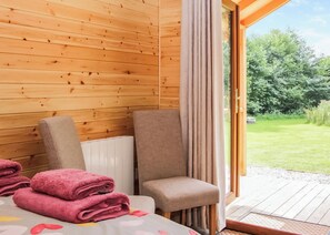 Una habitación con paredes de madera, una cama con cabecera blanca, dos sillas y vista a un jardín por una puerta de cristal.