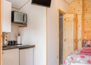 Ein kleines Zimmer mit Küchenzeile, einem Bett mit floralem Bettbezug, einer Holzwand und einem an der Wand montierten Fernseher.