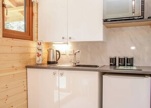 Una cocina con paredes de madera, un hervidor de acero inoxidable, un microondas y un lavamanos.