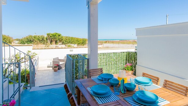 A balcony with a table set for dining, overlooking a beach and the sea. - Cosy apartment for 5 people with A/C, WIFI, TV and veranda, close to Ostuni (Pantanagianni-pezze Morelli)