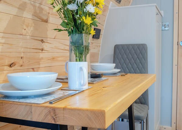 Une table de salle à manger en bois, avec des bols blancs, une tasse blanche et un vase rempli de fleurs.