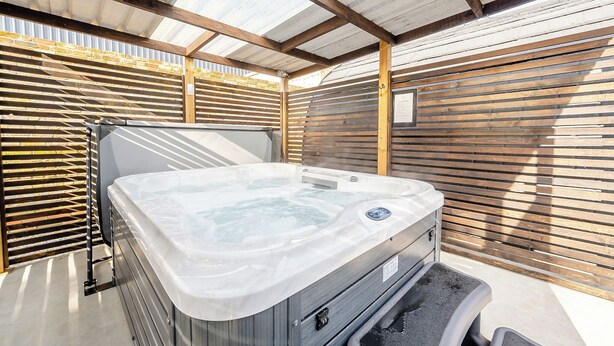 Un bain à remous situé dans un espace extérieur abrité, avec des lambris en bois et des poutres métalliques.