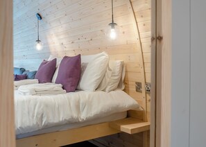 A wooden-paneled room with a bed, pillows, and a bedside table.