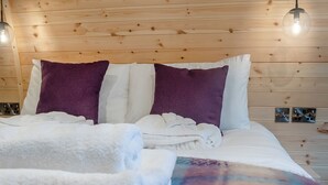 Un lit avec une literie blanche et violette, des murs recouverts de panneaux en bois et une prise électrique visible.