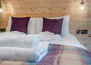 A bed with white and purple bedding, wooden panel walls, and a visible electrical outlet. - 1 bedroom accommodation in Wangford, near Southwold (Wangford, near Southwold)