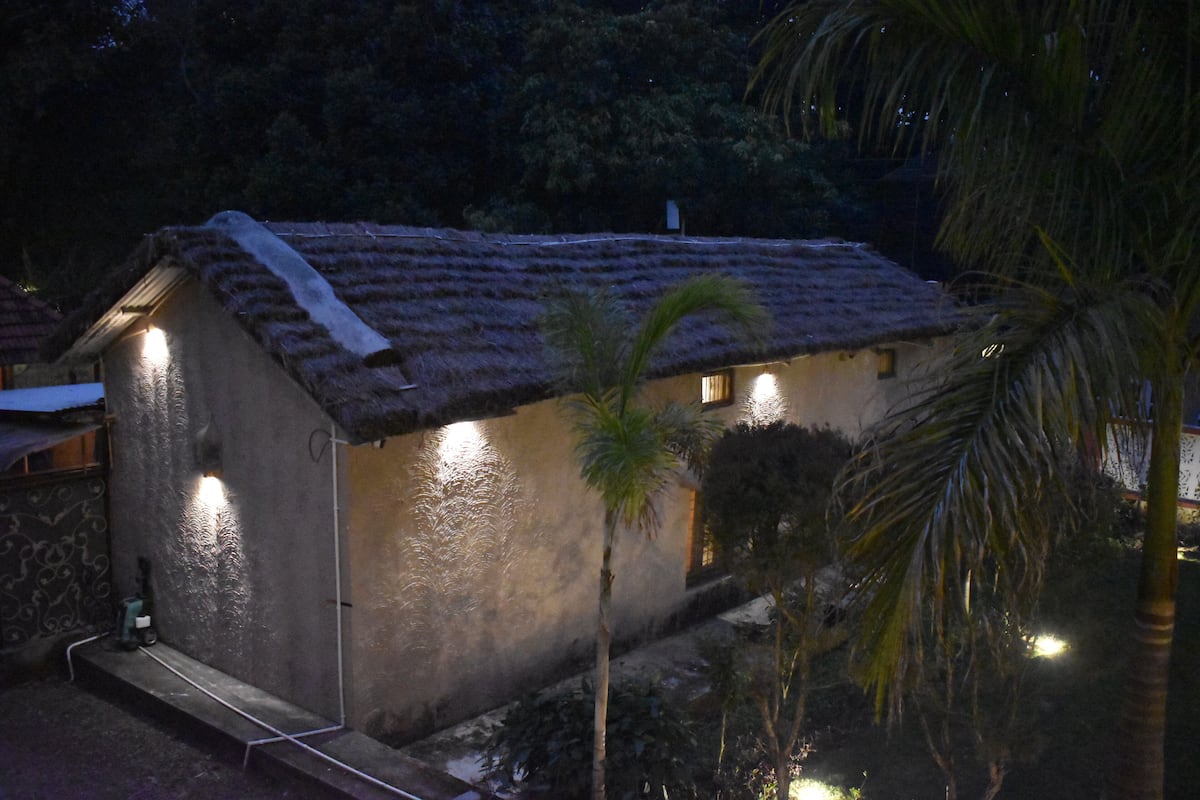 A small, single-story building with a thatched roof, surrounded by palm trees and vegetation.