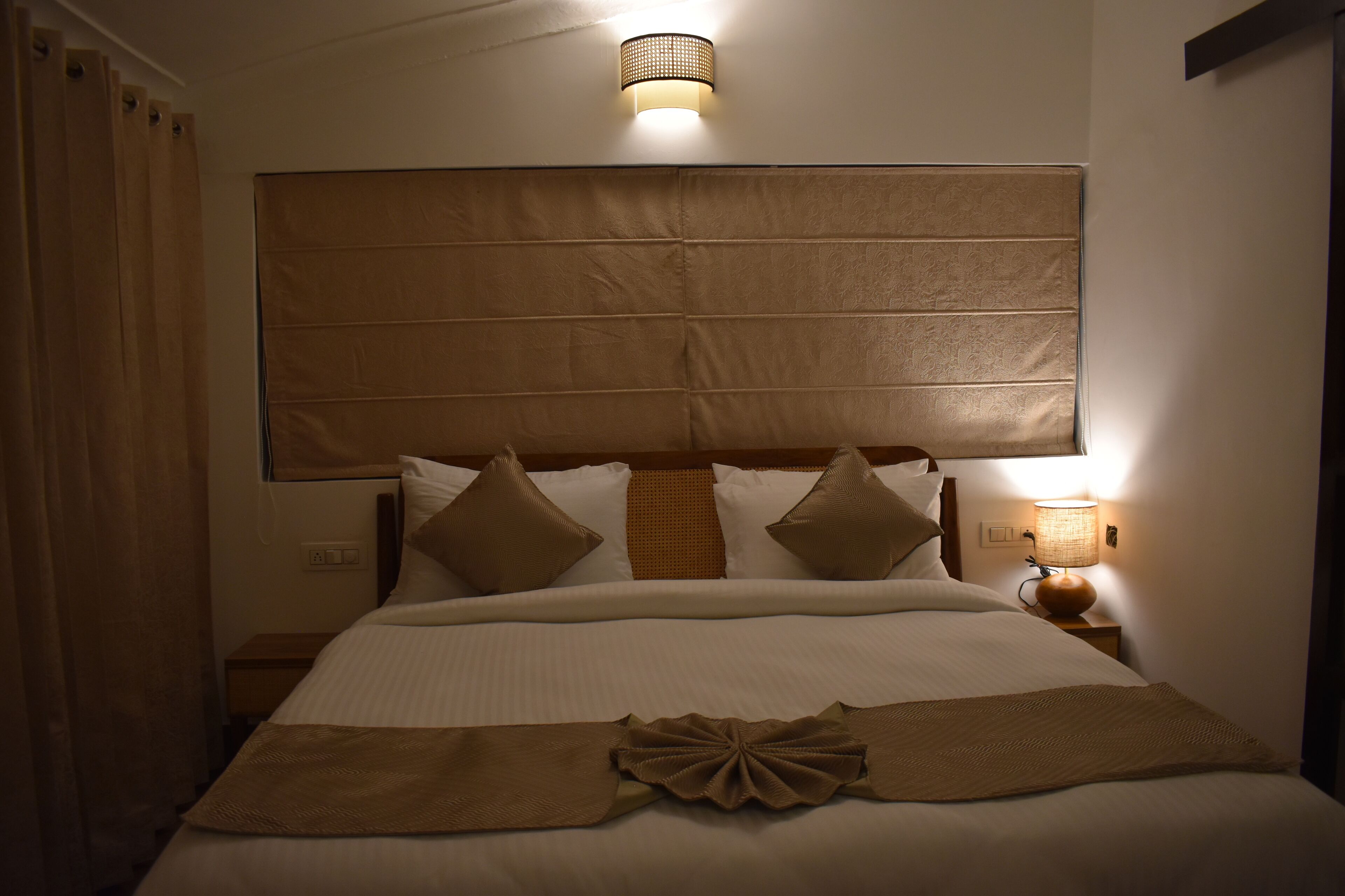 Une chambre d’hôtel avec un grand lit, une tête de lit, une lampe de chevet et un rideau.