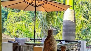 A covered outdoor area with hexagonal tiled flooring, a thatched roof, and a view of lush greenery. - 3 Acres Resort (Vikasnagar)