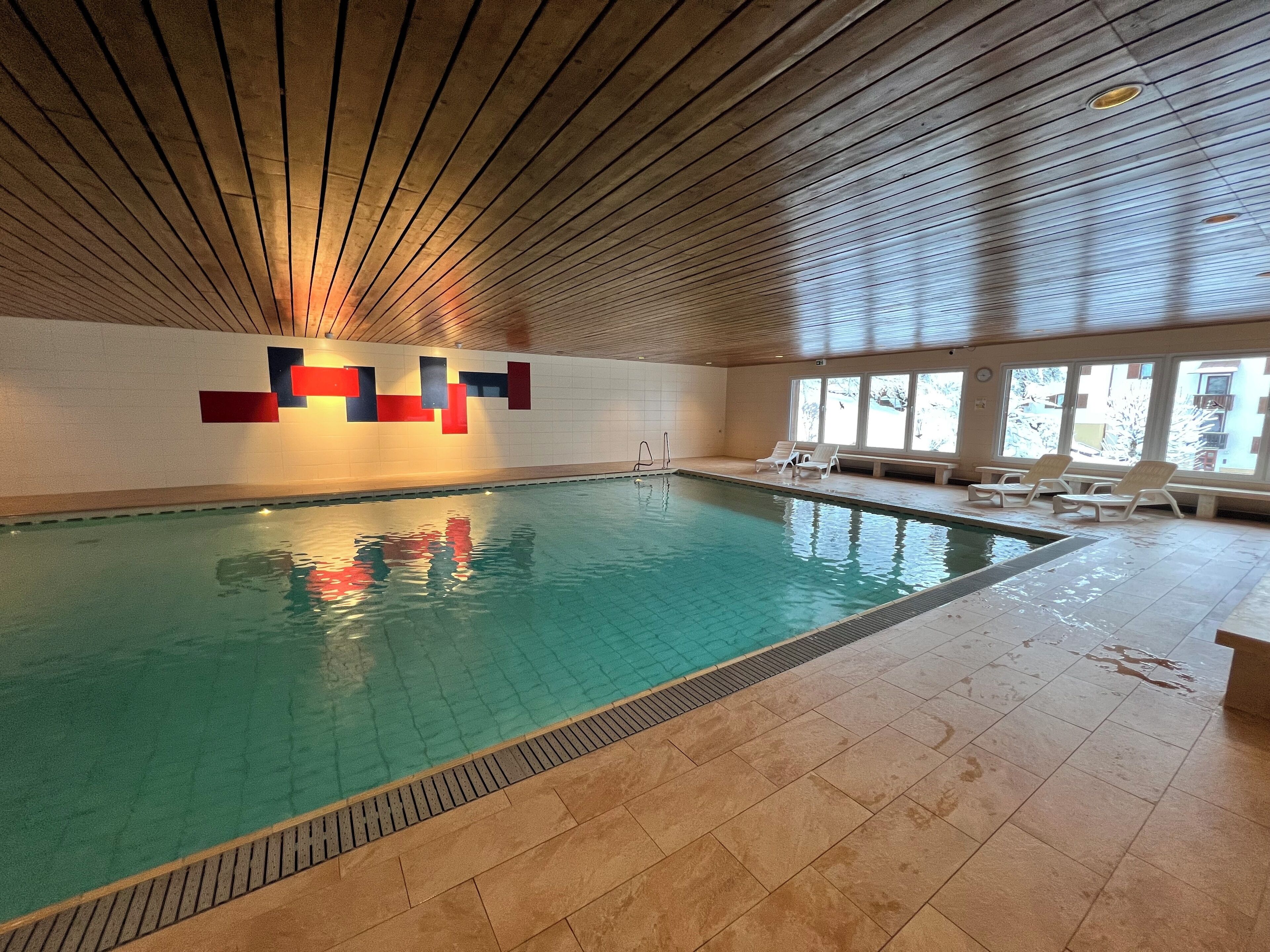 Een binnenzwembad met betegelde vloer, houten plafond en een muur met een geometrisch ontwerp.