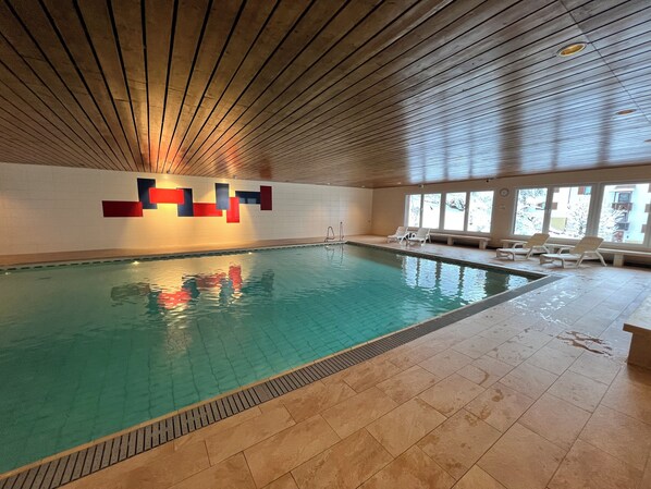 An indoor swimming pool with a tiled floor, a wooden ceiling, and a wall with a geometric design.