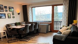 A modern living room with a dining area, large windows, and a view of the outdoors.