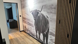 A hallway with a wooden floor, a wall mural of a yak, and a door leading to a room with a bed and a desk.