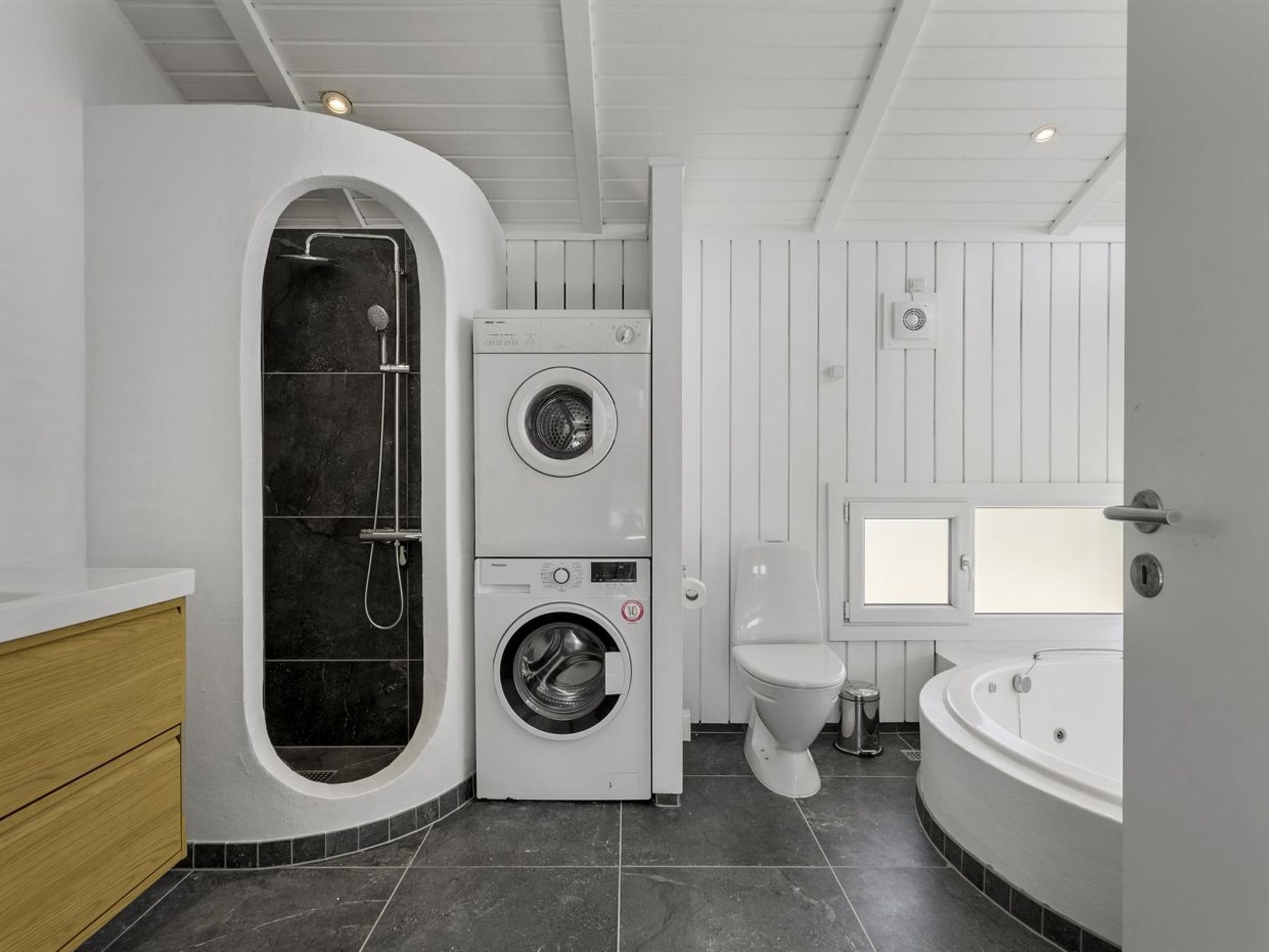 Un baño moderno con lavadora y secadora integradas, un inodoro separado y una bañera.