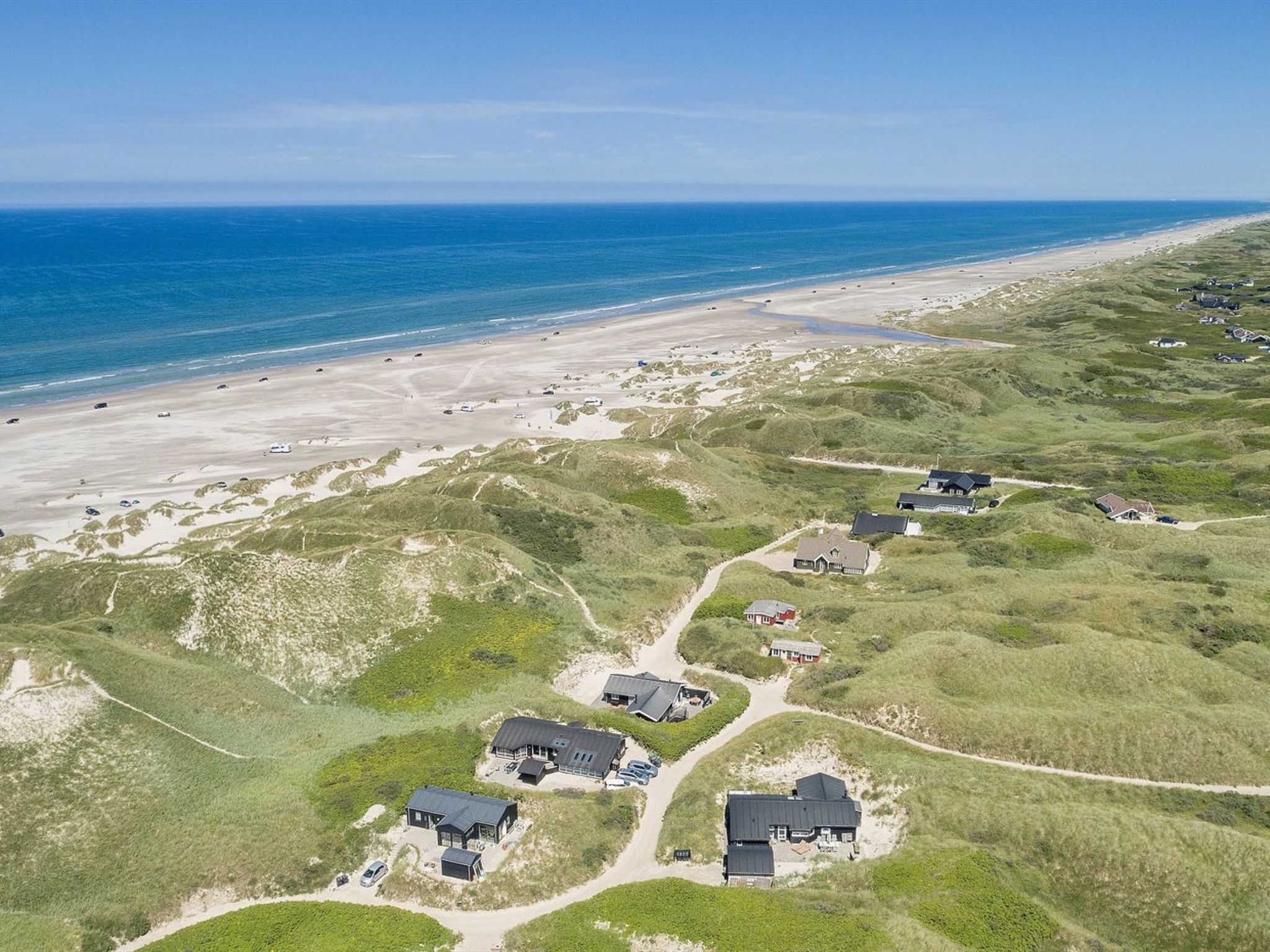 Vista aérea de una zona costera con varias casas, una playa y dunas.