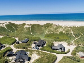 Luchtbeeld van een kustgebied met huizen, omringd door duinen, een strand en de oceaan op de achtergrond.