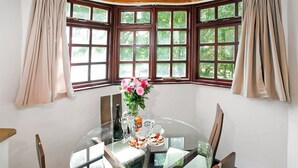 A round glass table with chairs, a vase of flowers, a bottle, glasses, and a box of tea. - The Summerhouse 2 Bed (Penzance)