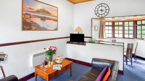 A room with a sofa, a coffee table with a vase of flowers, a clock, and a window with curtains. - The Summerhouse 2 Bed (Penzance)