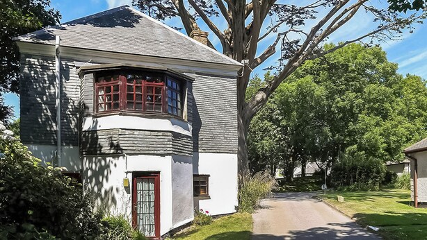 A two-story house with a sloped roof, a bay window with red shutters, and a red door. - The Summerhouse 2 Bed (Penzance)