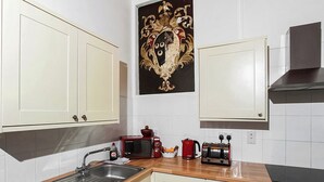 A kitchen with white cabinets, a wooden countertop, a red microwave, a kettle, and a toaster. - The Summerhouse 2 Bed (Penzance)