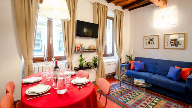 A dining area with a red table, chairs, and a glass coffee table. There is a blue sofa with orange cushions in the living area. - Apartment Historical Center Florence (Firenze)