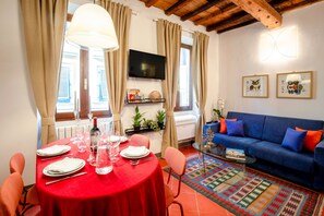A dining area with a red table, chairs, and a glass coffee table. There is a blue sofa with orange cushions in the living area.