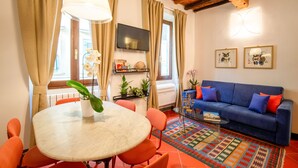 A living room with a blue sofa, orange chairs, a round table with a plant, and a TV mounted on the wall. - Apartment Historical Center Florence (Firenze)