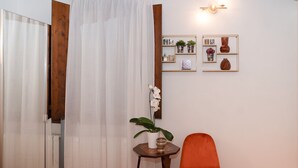 A room with a wooden door, a white curtain, a small table with a potted plant, an orange chair, and wall-mounted decor including a mirror and framed pictures. - Apartment Historical Center Florence (Firenze)