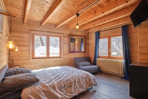 Ein Schlafzimmer einer Holzhütte mit einem Bett, einem Sessel, einer Heizung und einem Fernseher.