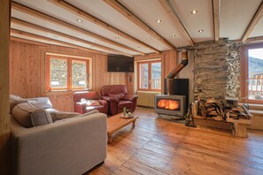 Un intérieur en bois avec un canapé, un fauteuil, une cheminée et un mur en pierre.