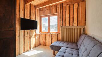 A wooden interior with a flat-screen TV mounted on the wall, a window, and a sofa.