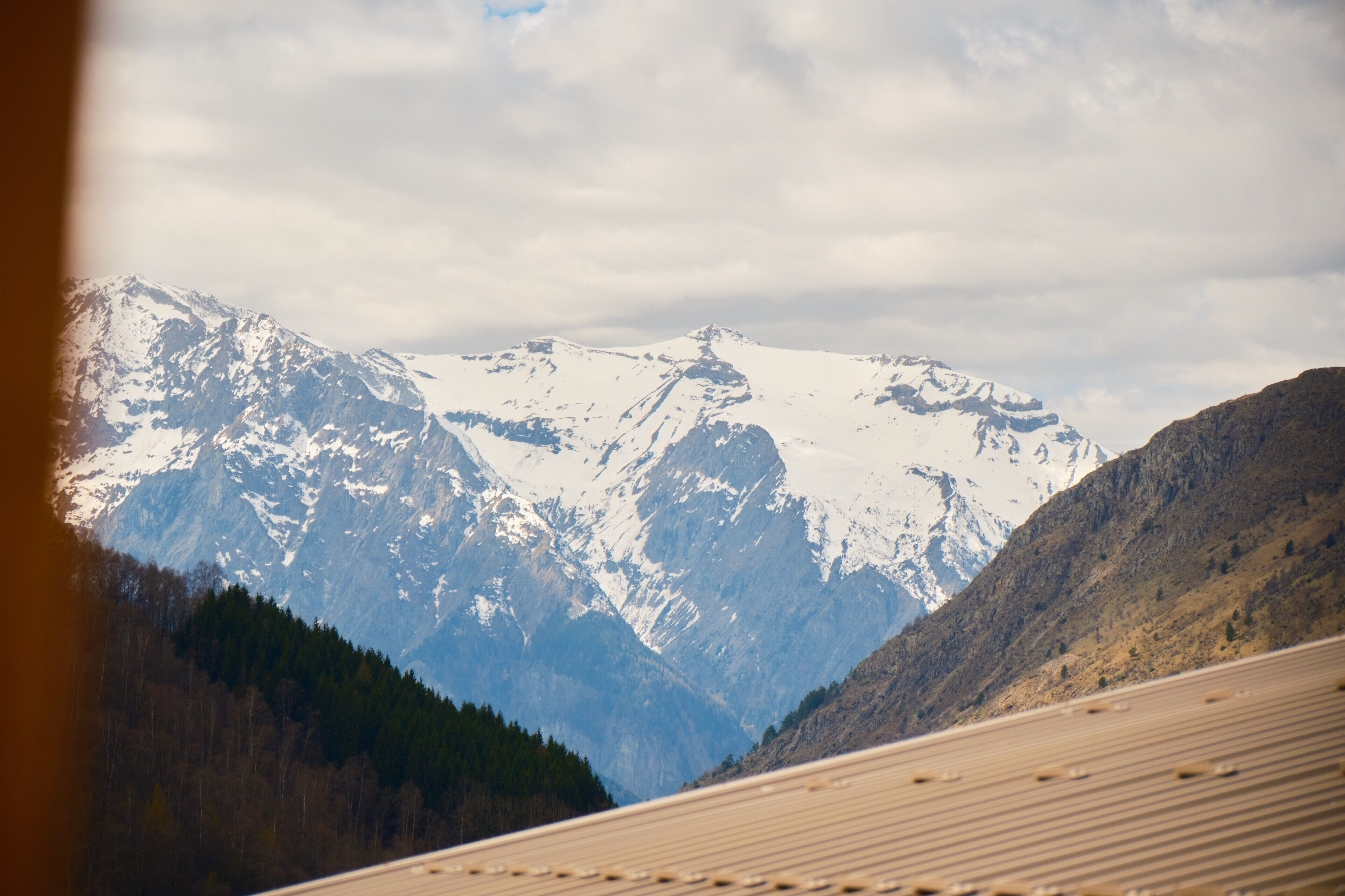 Un paysage de montagne avec des sommets enneigés et une vallée boisée.