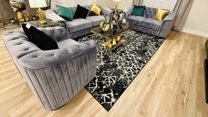 Ein Wohnzimmer mit zwei grauen Sofas, einem schwarz-weißen Teppich und einem goldenen Couchtisch.