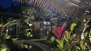A well-lit outdoor area with a thatched roof, a hanging light fixture, and a variety of tropical plants. - Widji Garden Villa (Pecatu)