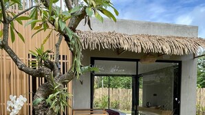 A modern house with a thatched roof, a glass door, and a garden with various plants and a wooden deck. - Widji Garden Villa (Pecatu)