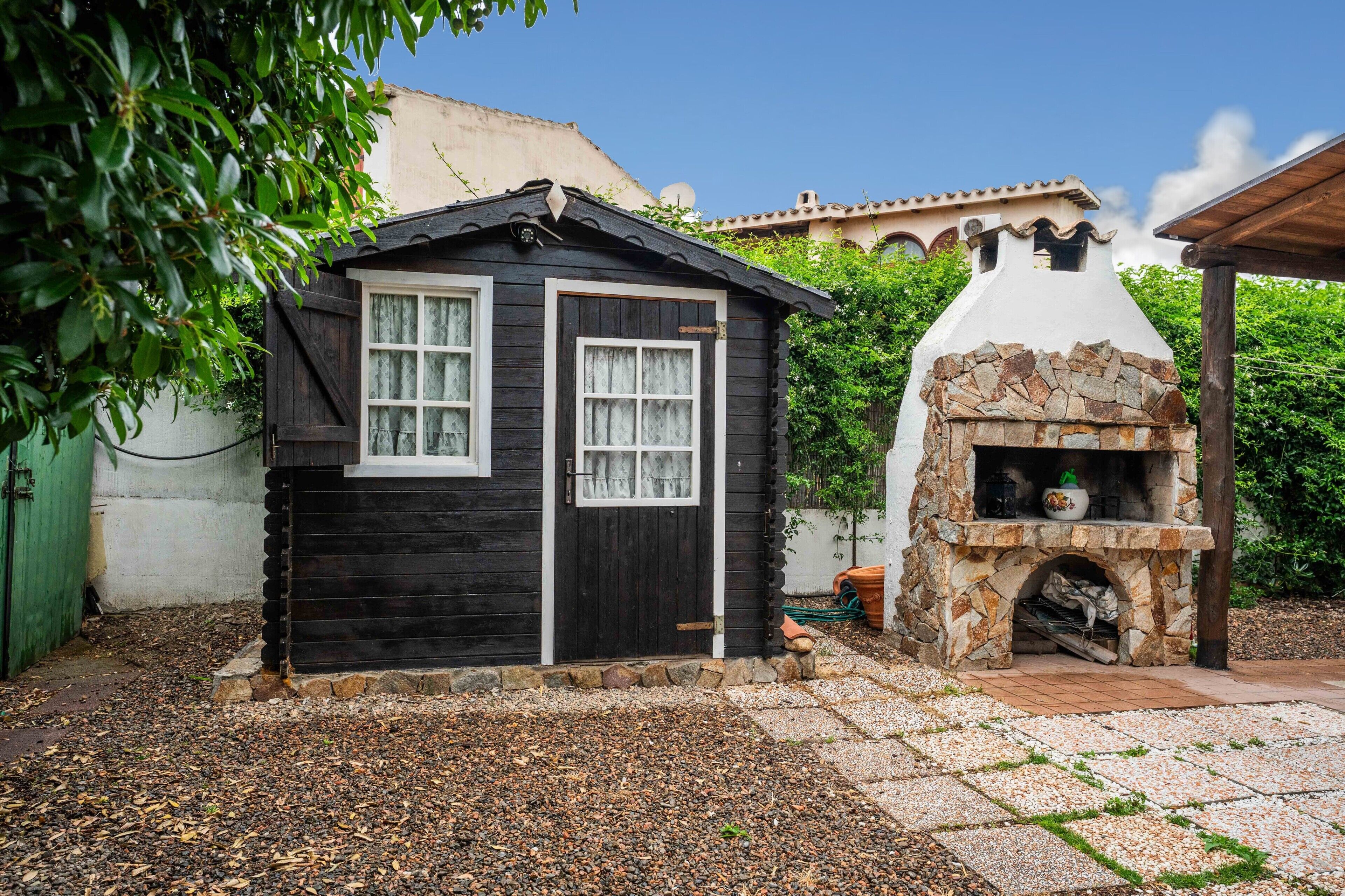 Eine kleine Holzhütte mit Kamin aus Stein, umgeben von einem Garten mit Kieswegen.