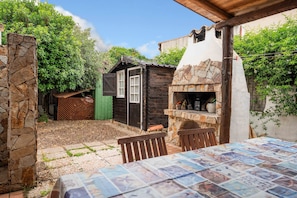 Un espace patio comprenant une table, des chaises, un mur en pierre et une petite construction en bois dotée d’une cheminée.