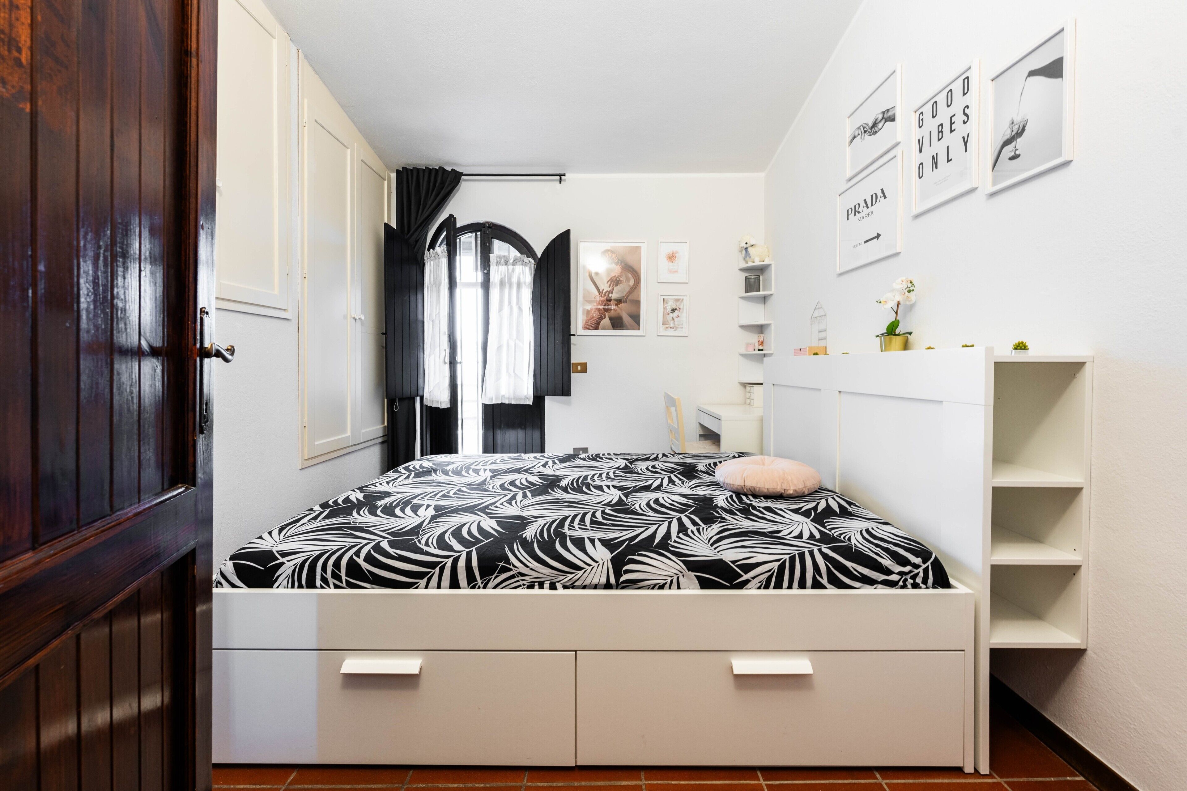 Un dormitorio con cama, armario, escritorio y estante con objetos decorativos.