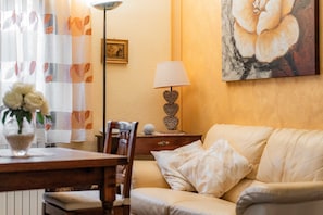 Un salon avec un canapé, une table ornée d’un vase de fleurs, une lampe et un tableau accroché au mur.