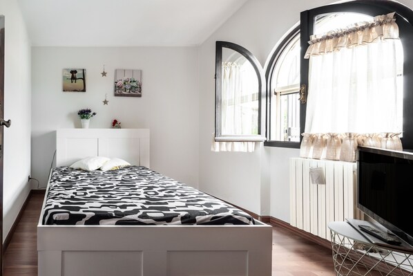 Une chambre à coucher avec un lit, une télévision, un radiateur et une fenêtre avec des rideaux.