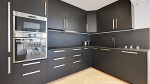 A modern kitchen with dark cabinetry, stainless steel appliances, and a view of the outdoor seating area. - Charming Apt with AC & balcony (Suresnes)