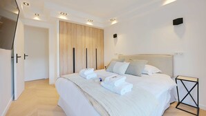 A modern bedroom with a large bed, a wooden wardrobe, and recessed ceiling lights. - Charming Apt with AC & balcony (Suresnes)