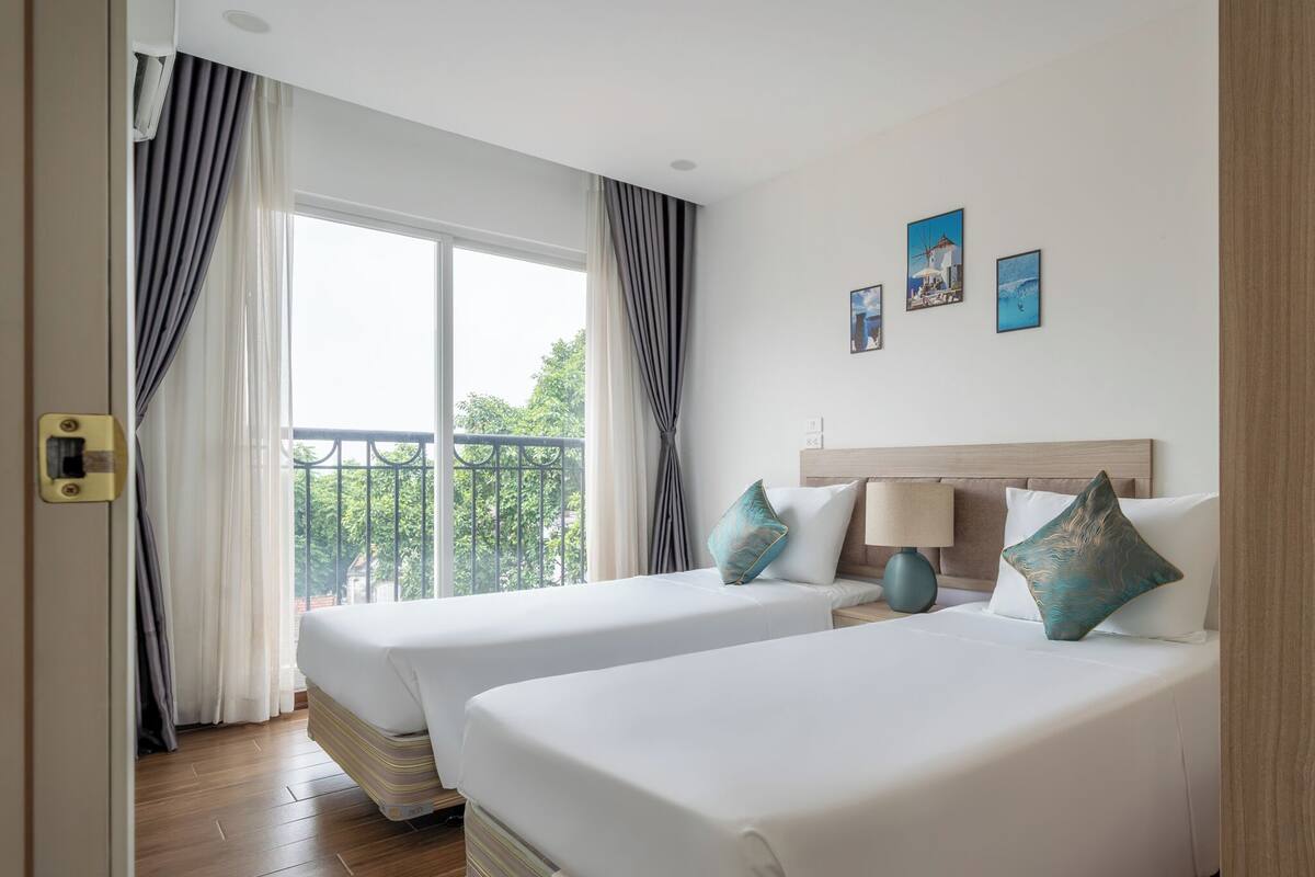 A hotel room with two beds, a balcony, and a view of greenery.
