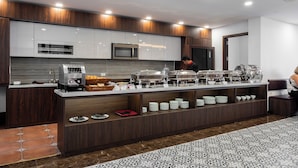 Een moderne keuken met een buffetopstelling, inclusief een koffieapparaat, buffetkommen en een magnetron.